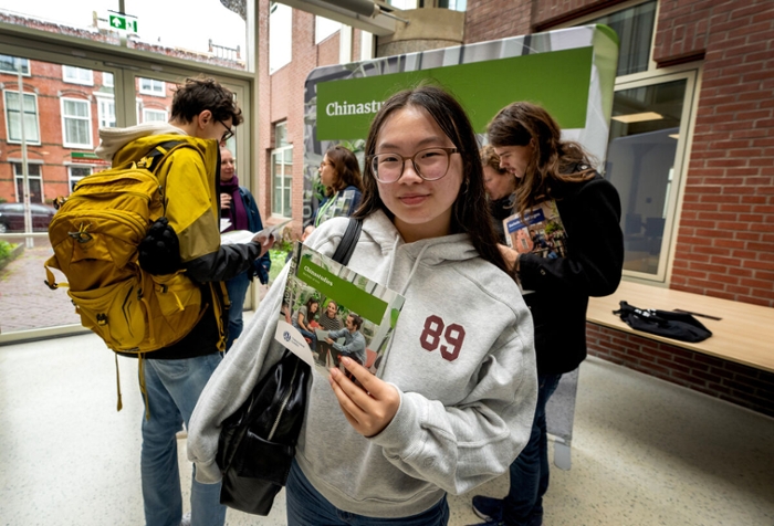 A girl wearhing glasses and a grey hoodie holds a Chinese Studies leaflet.
