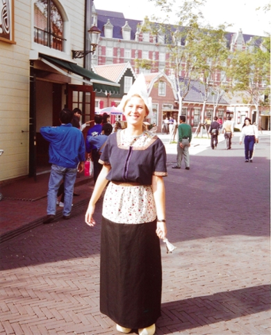 A woman in Dutch national costume with a white cap on her head and holding a bell.