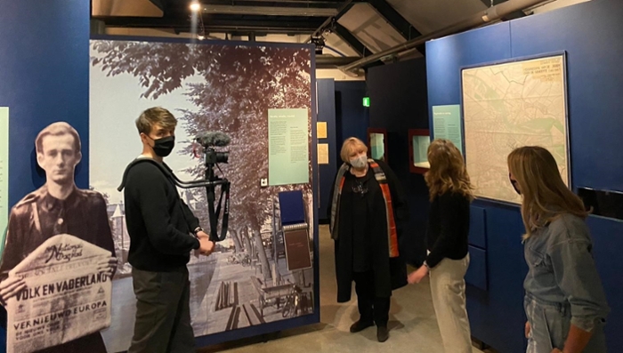 Two students interview Dubravka Ugrešić by an exhibit at the Resistance Museum while a third student films them.