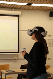 A young woman with dark hair and dark clothes is wearing a white pair of VR-goggles
