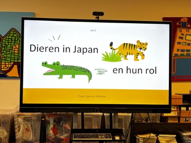 A screen in a classroom showing a drawing of a tiger and a crocodile with the text: Animals in Japan and their role.