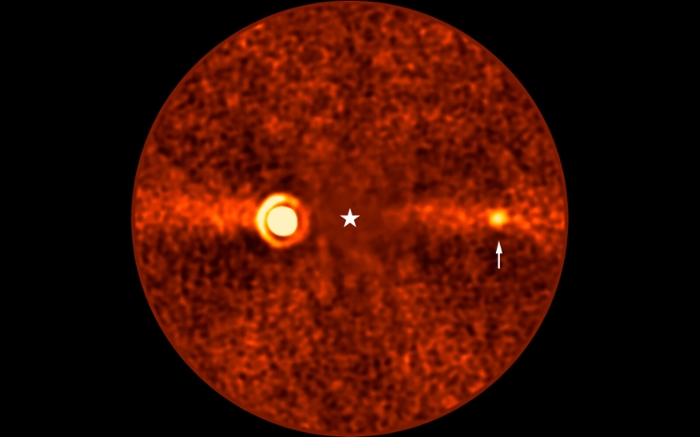The newly discovered planet Beta Pictoris d (indicated by the white arrow) in an image captured by the Very Large Telescope. The light from the star Beta Pictoris has been blocked out (at the position marked by the white star). The much larger planet Beta Pictoris b is visible on the left. © ESO/B. Sutlieff, M. Bonse et al.